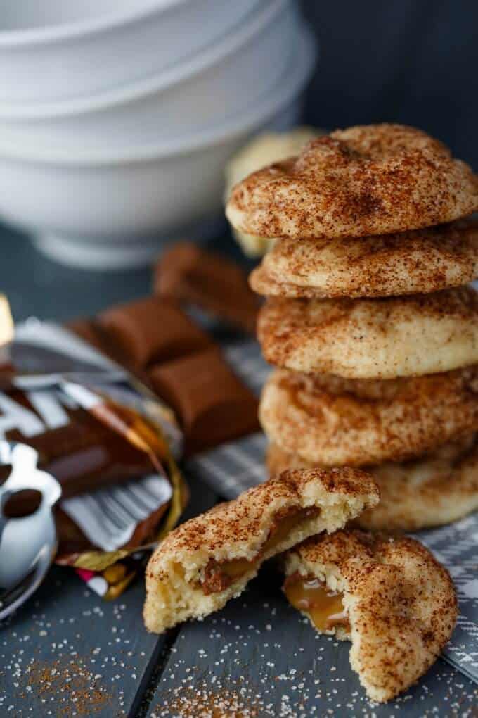 Caramilk Stuffed Snickerdoodles on gray table with chocolate, spoon and white bowls in the background