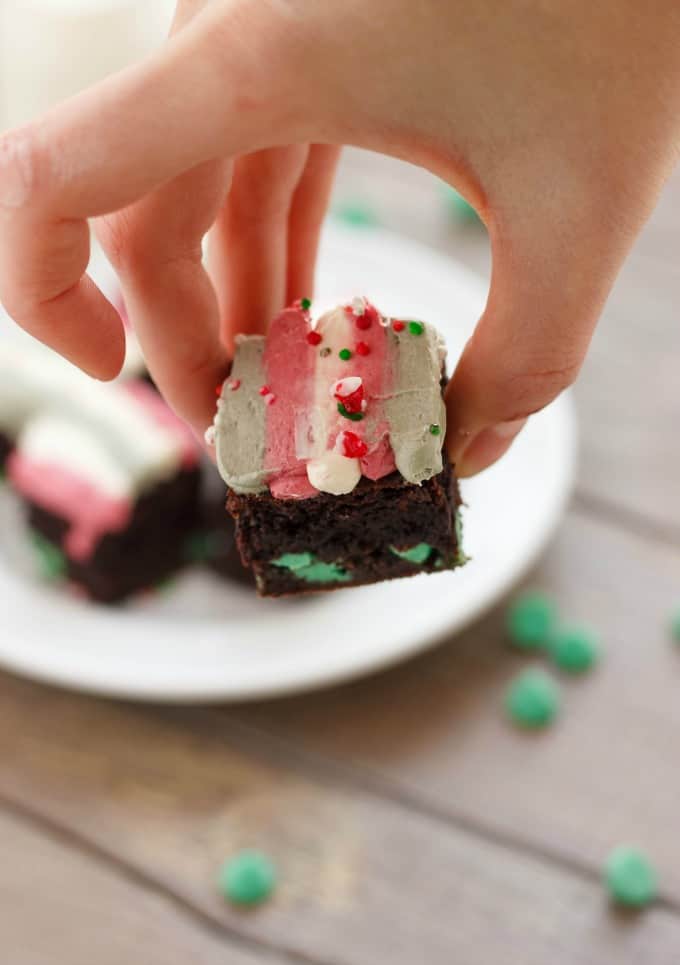 Christmas Brownies (Mint Chocolate Brownies)  held by hand, plate with brownies on wooden table in the background#brownies