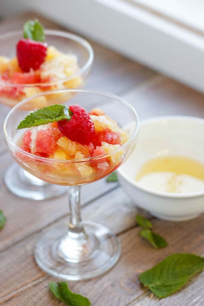 Fresh Fruit Salad using Leftover Fruit and Simple Syrup in glass cups on wooden table with white bowl and herb leaves