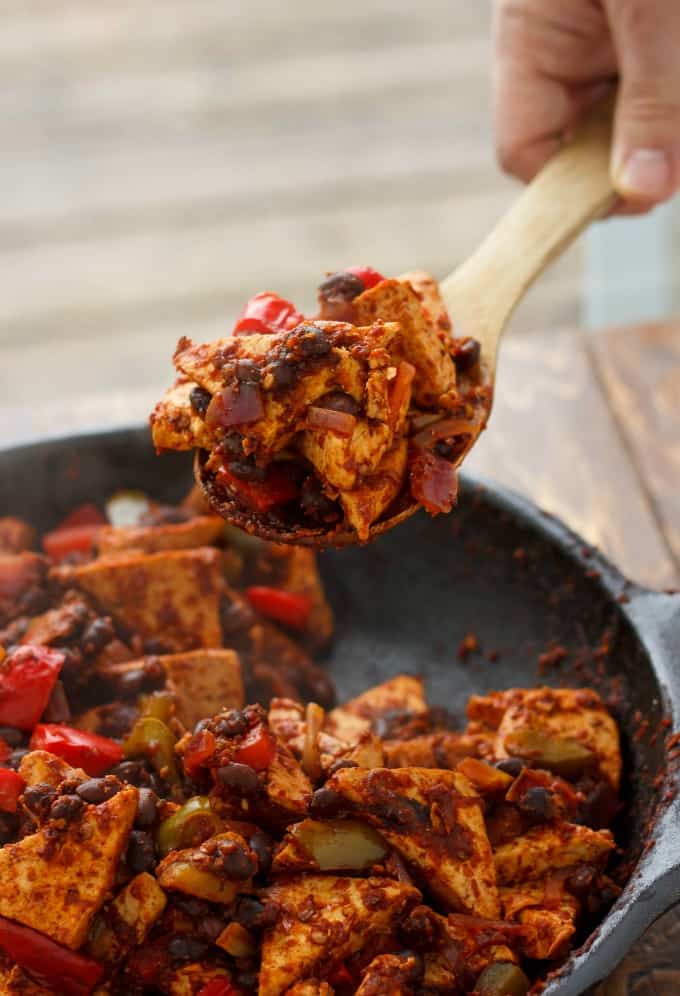 Spicy tofu quinoa in black pan picked up by wooden spatula