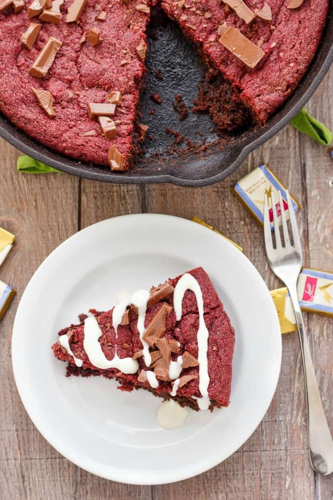 Cast Iron Giant Red Velvet Cookie Skillet in black pan and on white plate with spoon and spilled candy on wooden table