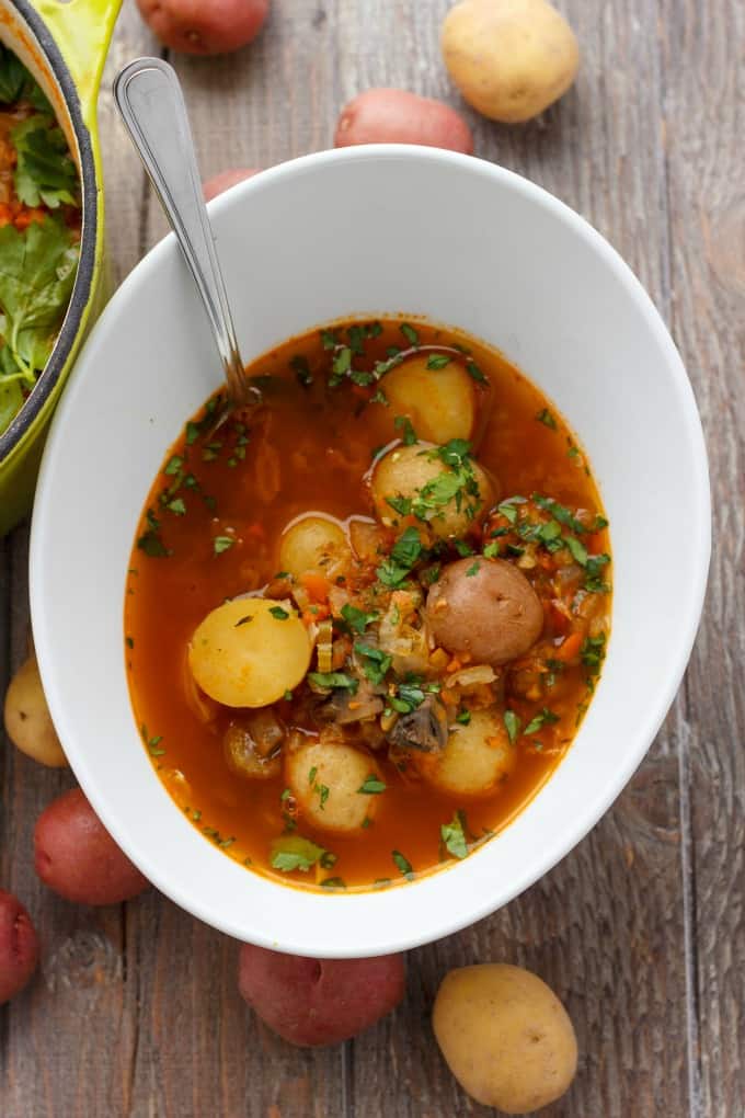 Simple Vegetable Soup with Creamer Potatoes in white bowl with spoon on wooden table with spilled potatoes around