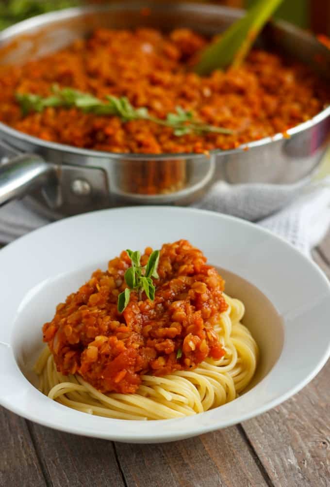 Vegetarian Lentil Bolognese Sauce with spaghetti on white plate and pan with green spatula with same sauce in the background