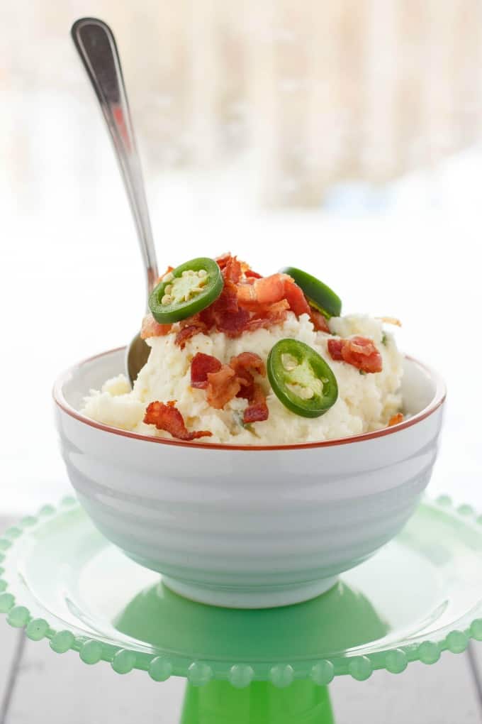 Jalapeno Popper Mashed Potatoes in white bowl with spoon on green tray