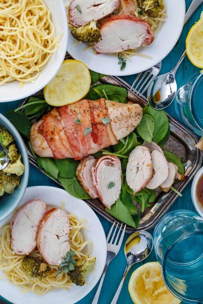 Bacon Wrapped Lemon Pepper Chicken Pasta on tray and white plate on blue table with spoon, forks and glass cups