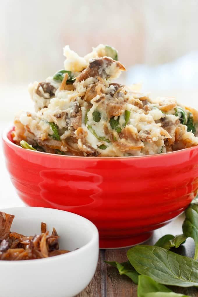 Caramelized Onions and Mushroom Mashed Potatoes in red bowl with white bowl with mushrooms and herb leaves on table #potatoes