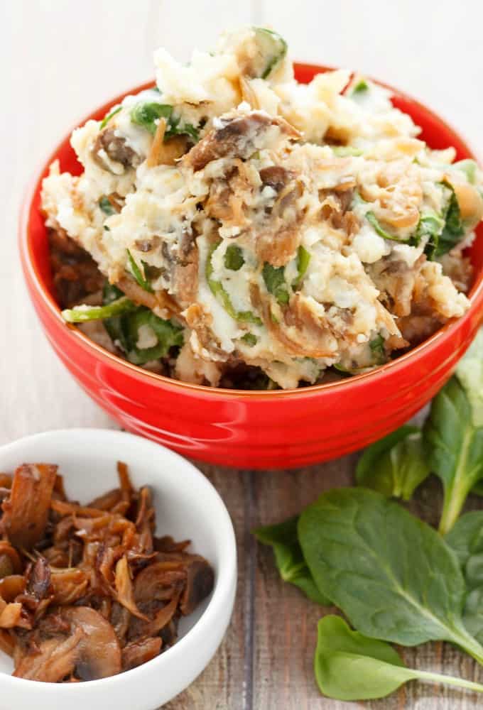 Caramelized Onions and Mushroom Mashed Potatoes in red bowl on wooden table with herb leaves and white bowl with mushrooms #sidedish