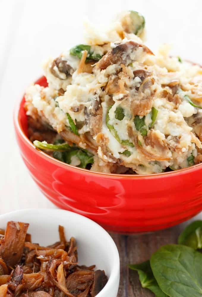 Caramelized Onions and Mushroom Mashed Potatoes in red bowl on wooden table with herb leaves and white bowl with mushrooms#vegetarian