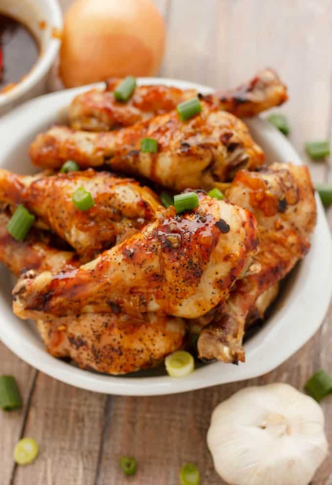 Honey Garlic Chicken Drumsticks in white bowl next on wooden table with chopped veggie and garlic#chicken