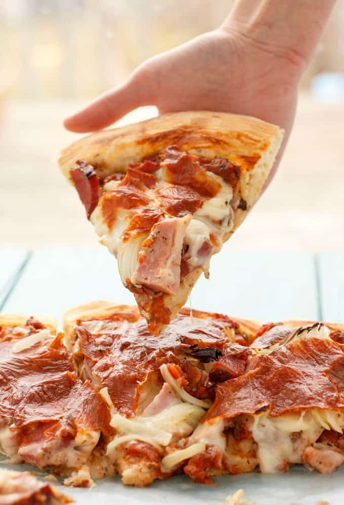 Leftover Ham Pizza  slices on tray, slice held by hand