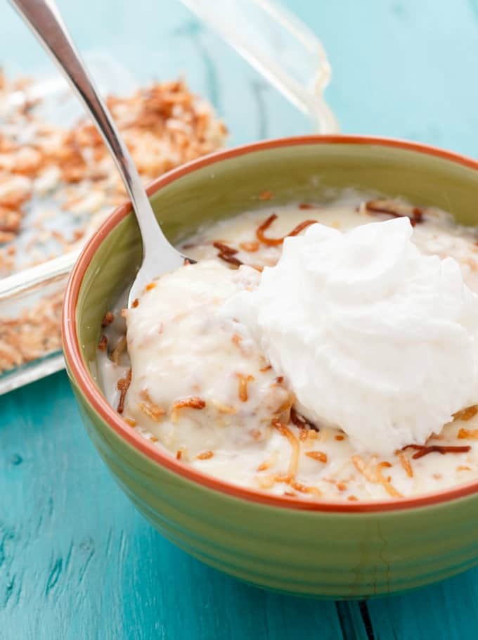 Homemade Toasted Coconut Pudding in green bowl with spoon and whipped cream