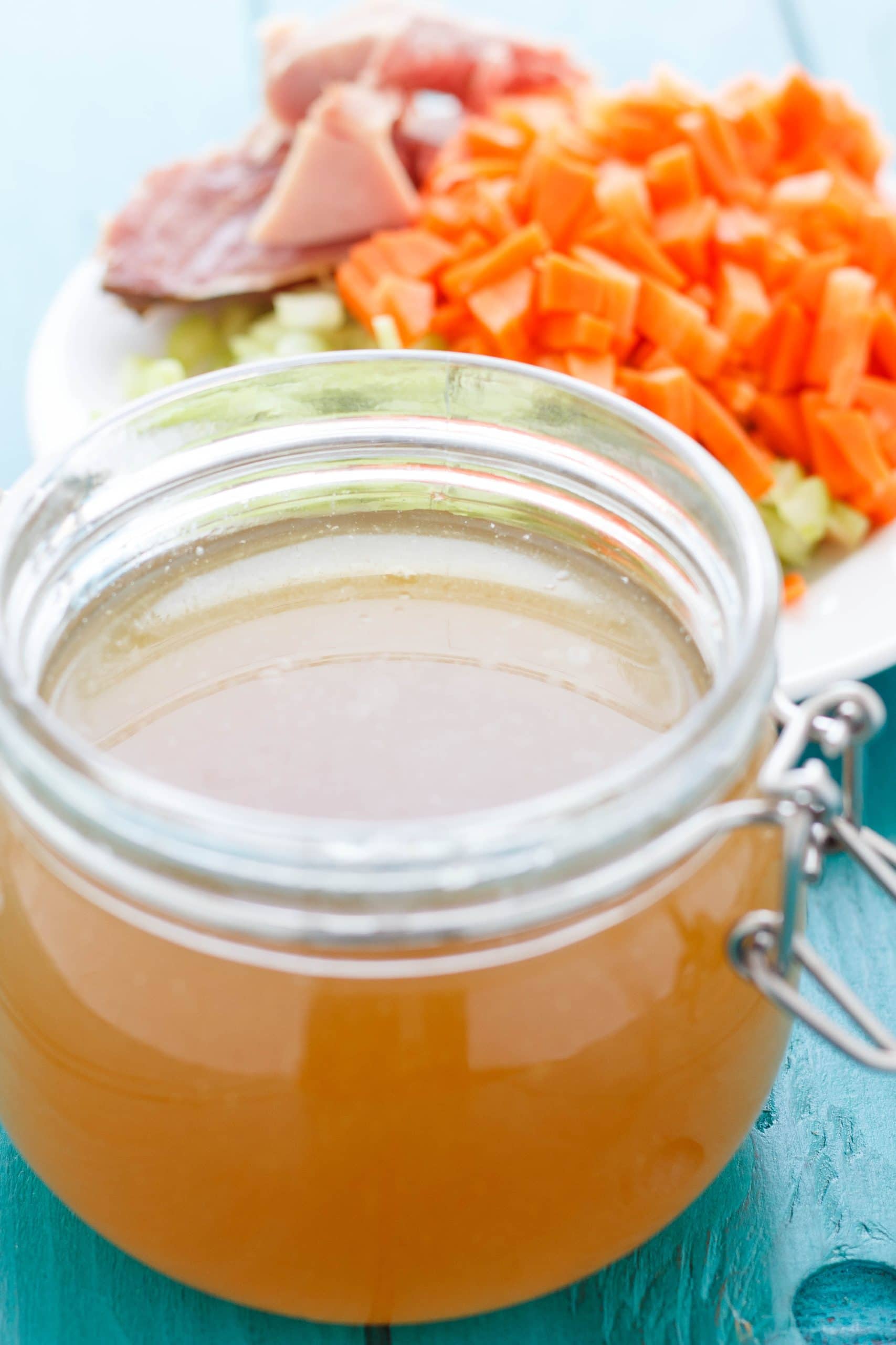 Homemade Ham Stock in glass ajr on blue table with plate full of vegetable