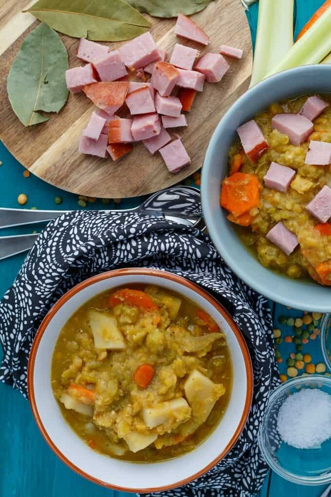 Slow Cooker Split Pea Soup with Ham in bowl, chooped ham on wooden pad with spoon and vegetable around