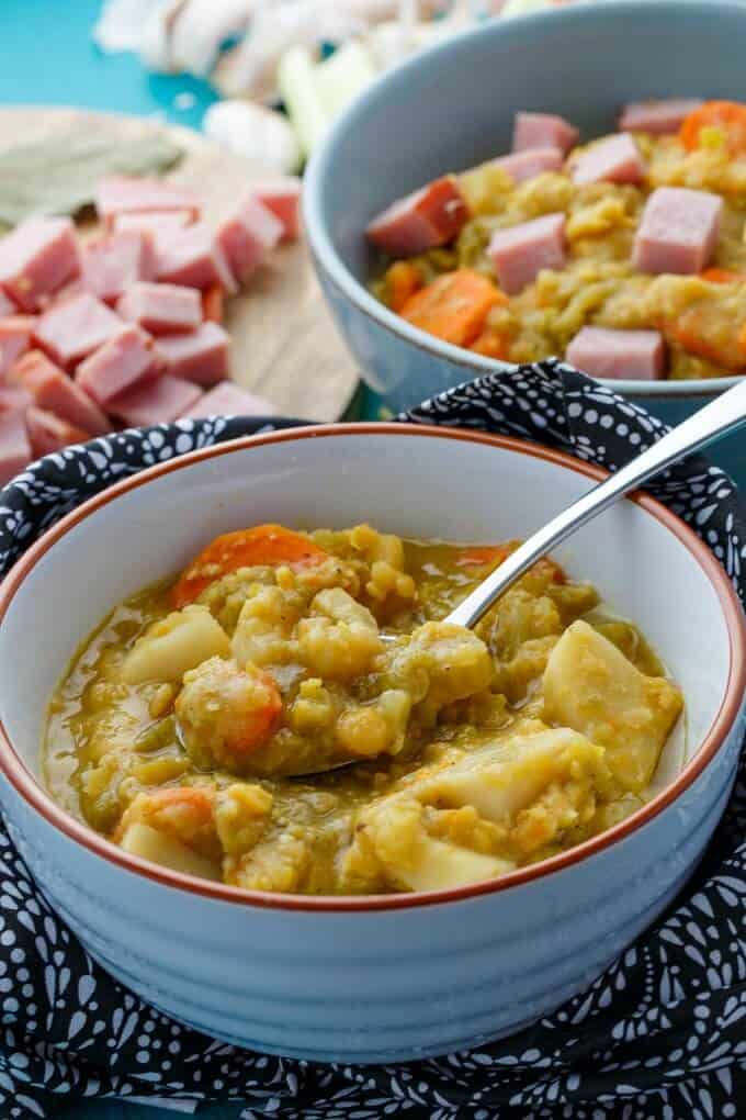 Slow Cooker Split Pea Soup with Ham in white bowls with spoon next to chopped ham on wooden pad