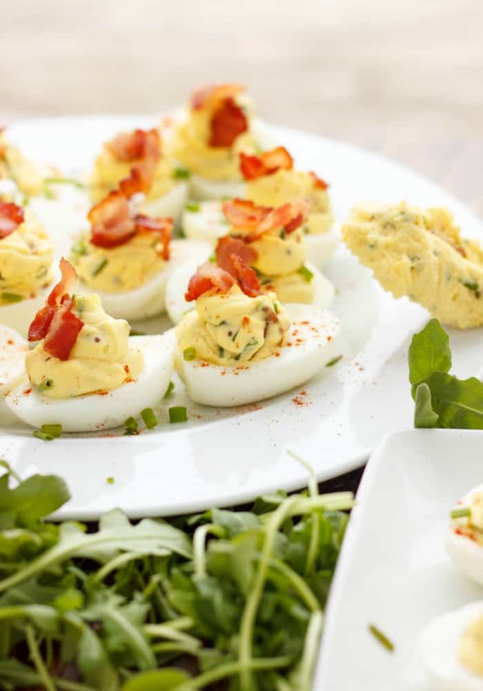 Sour Cream, Chive, and Bacon Deviled Eggs on white palte with herbs around #Easter