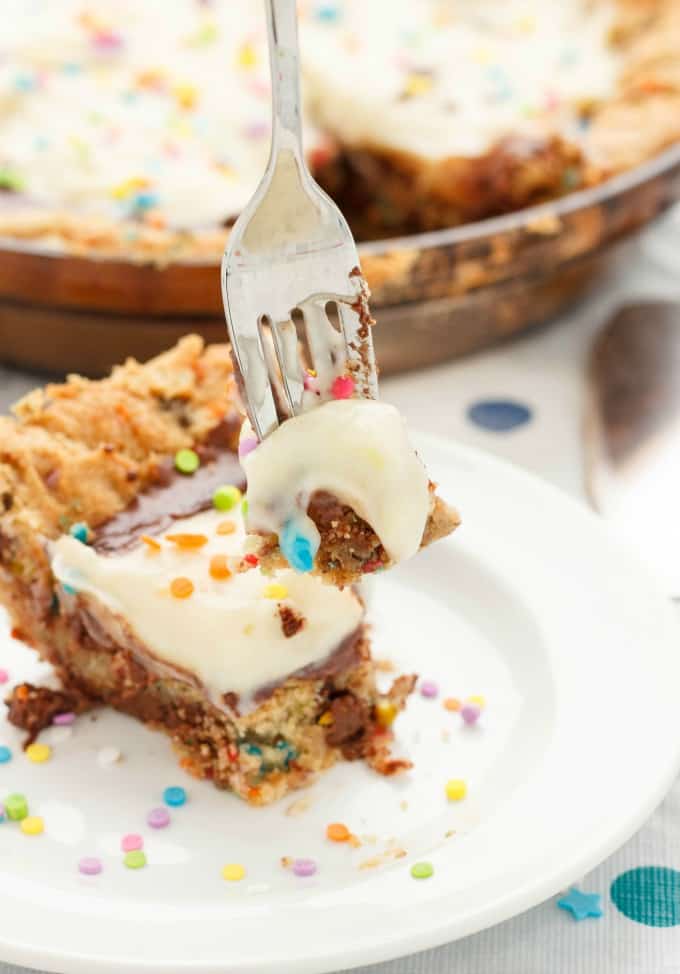 Bithday cake cookie and pudding pie on white plate picked by fork, rest of cake in the background