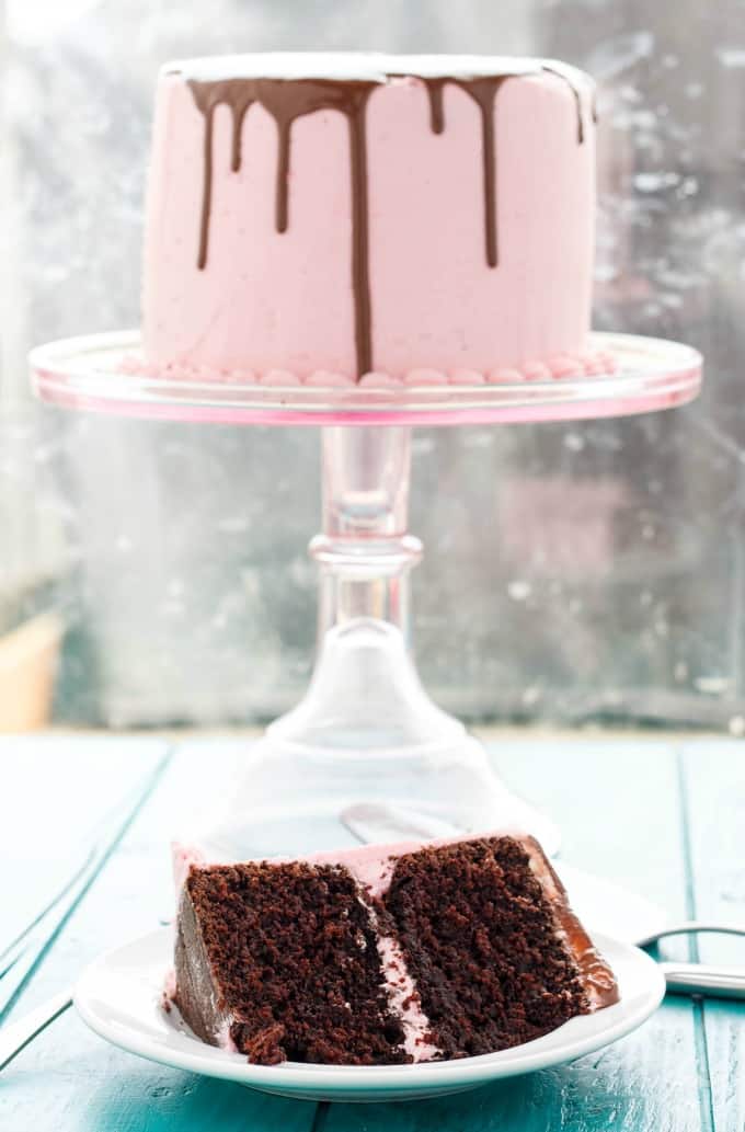 Chocolate Cake slice on white plate on blue table, whole pink cake on stray in the background #cake