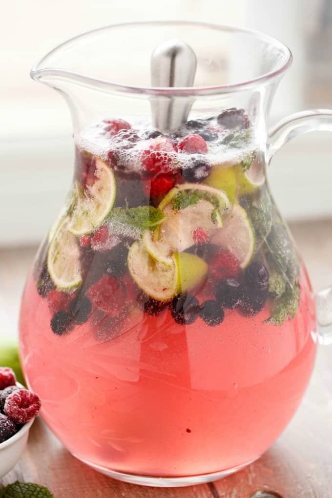 Mixed Berry Mojitos  with limes and berries in glass pitcher