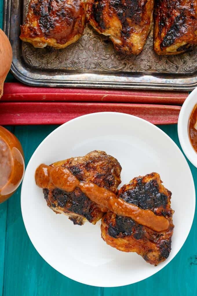 BBQ Chicken Thighs with Rhubarb BBQ Sauce on white plate and gray tray with rhubarb on blue table