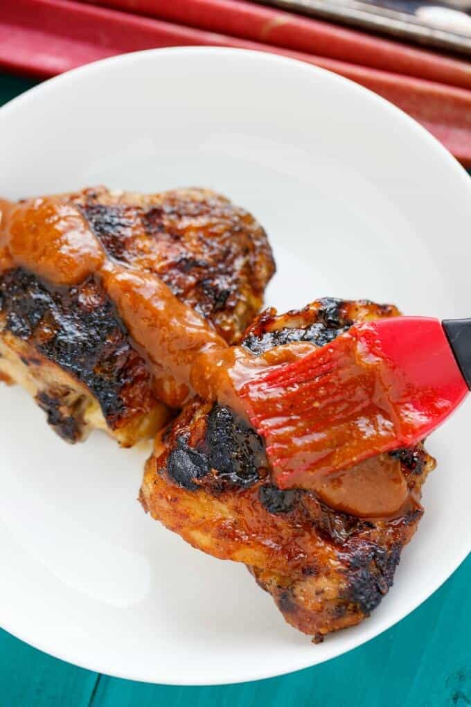 BBQ Chicken Thighs with Rhubarb BBQ Sauce on white palte with red brush and rhubarb on the table