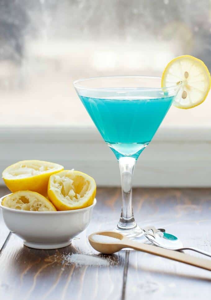 Catalina Margarita in glass cup with slcie of lemon on table with bowl of slcied lemons and spoons with salt