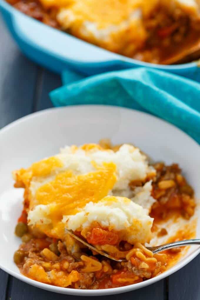 Shepherds pie with campbells soup cheese with fork on white plate, baking pot with blue cloth wipe in the background