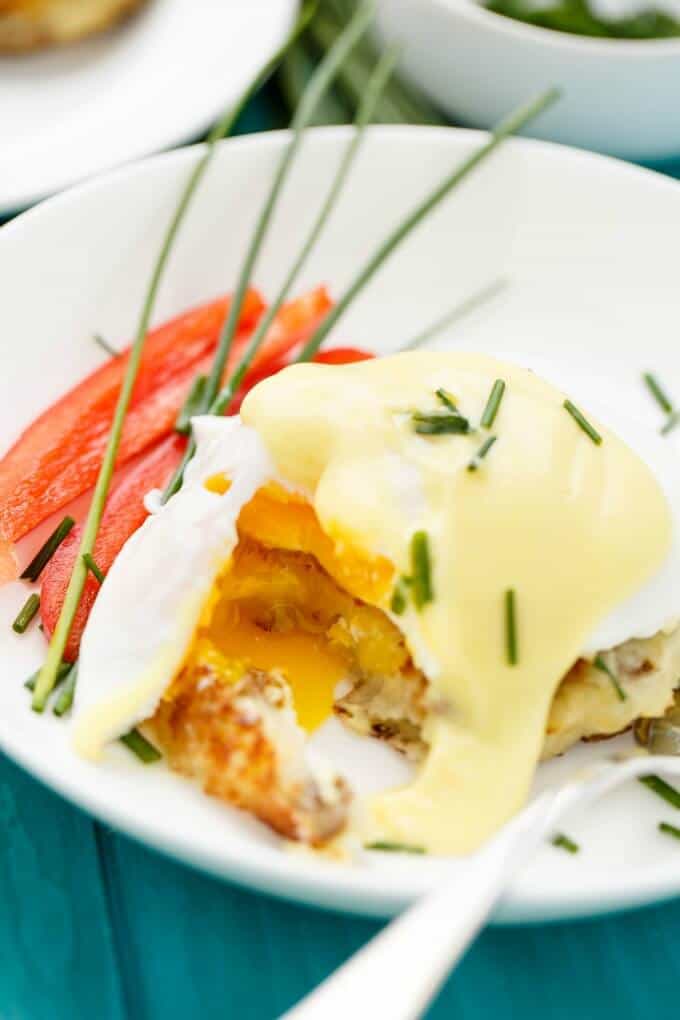 Eggs Benedict over Potato Pancakes on white plate with veggies and fork