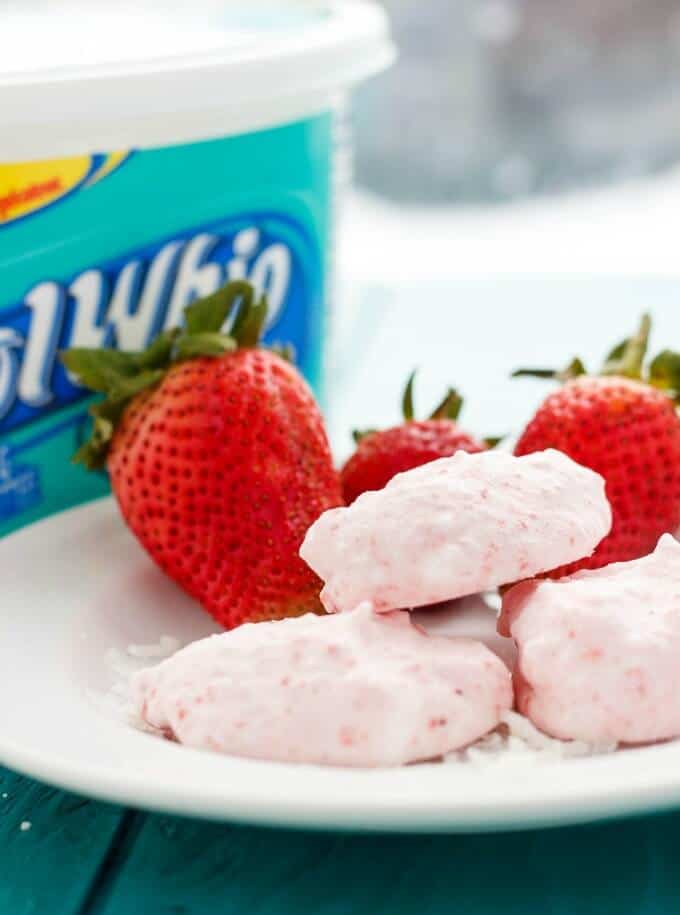 Three Ingredient Strawberry Frozen Bites on white plate with ripe strawberries, container in the background