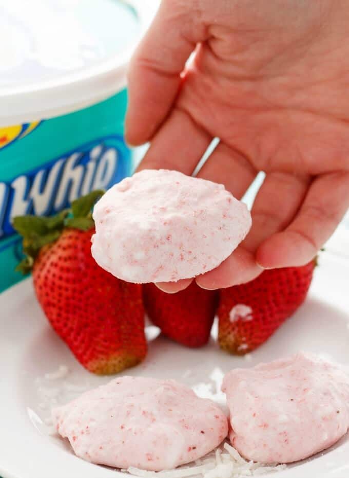 Three Ingredient Strawberry Frozen Bites held by hand on white plate with ripe strawberries