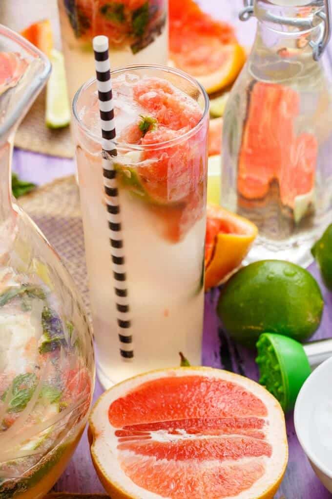 Broiled Grapefruit Mojito in the glass cup with straw and glass pitcher with graperfruits and limes on the table