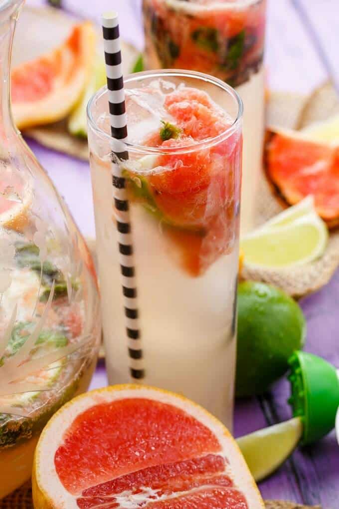 Broiled Grapefruit Mojito in glass up and glass pitcher with limes and grapefruits on the table