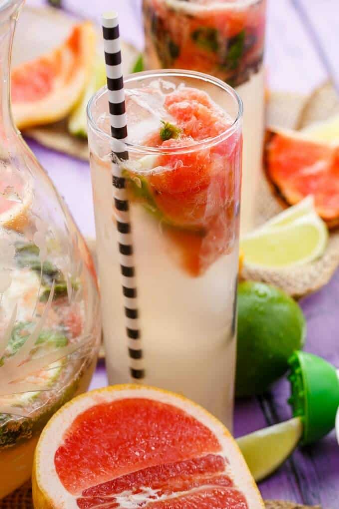 Broiled Grapefruit Mojitos in glass cup and pitcher wit hstraw, limes and grapefruits on the table