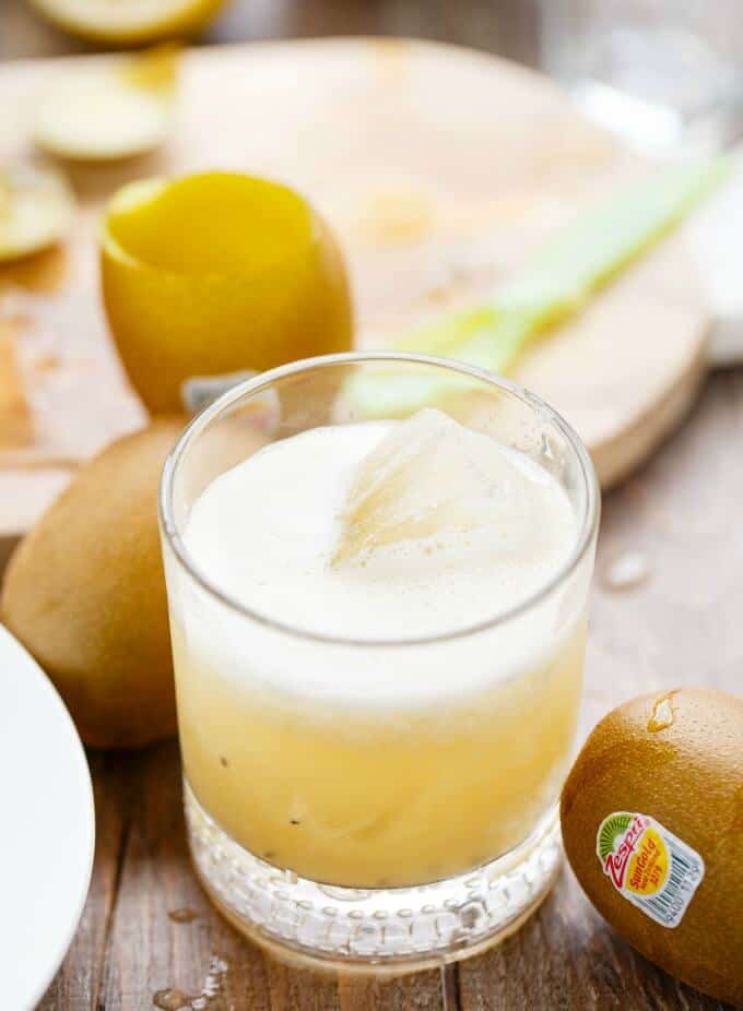 Kiwi Whiskey Sour drink with ice cube in glass cup with kiwis around