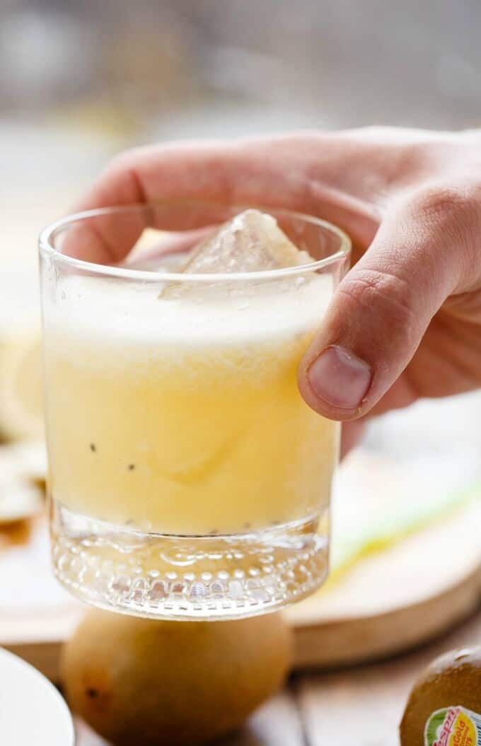 Kiwi Whiskey Sour drink with ice cube in glass cup held by hand