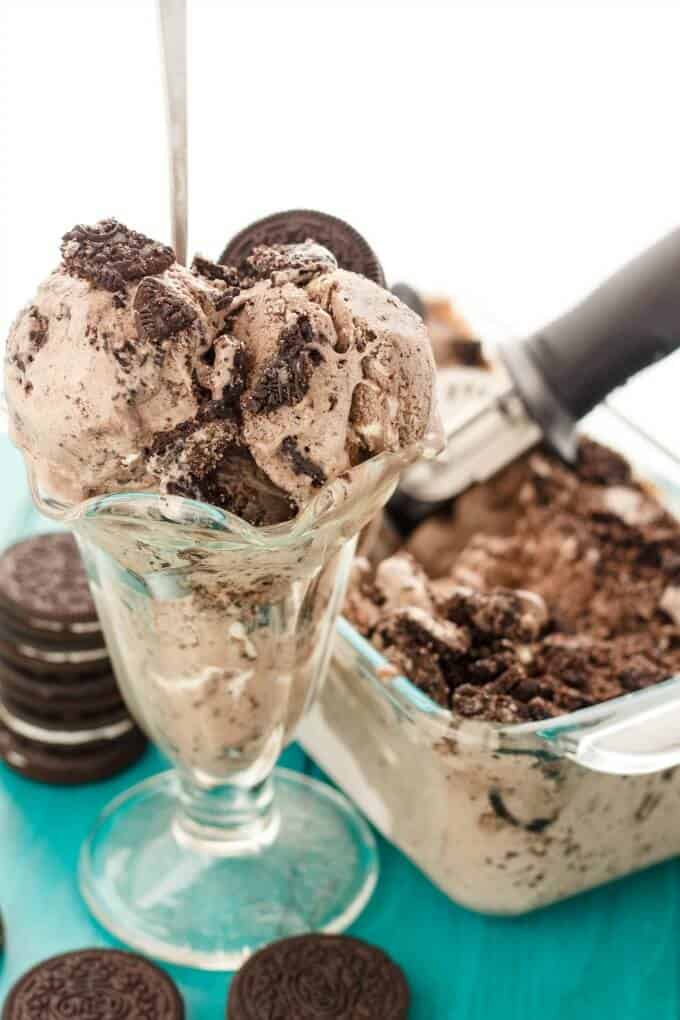 Oreos Cookies and Cream Ice Cream  in glass cup on blue table with oreos and ice cream container with scoop