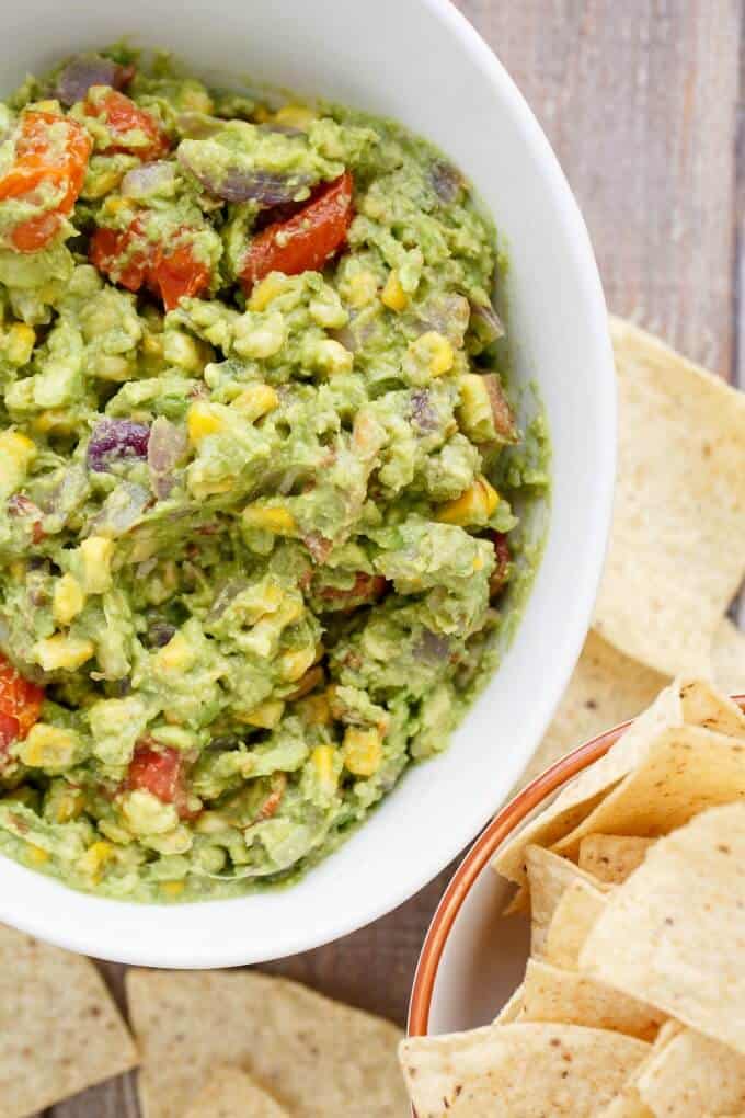 Roasted Guacamole with Bacon in white bowl next to bowl of chips, chips on gray table