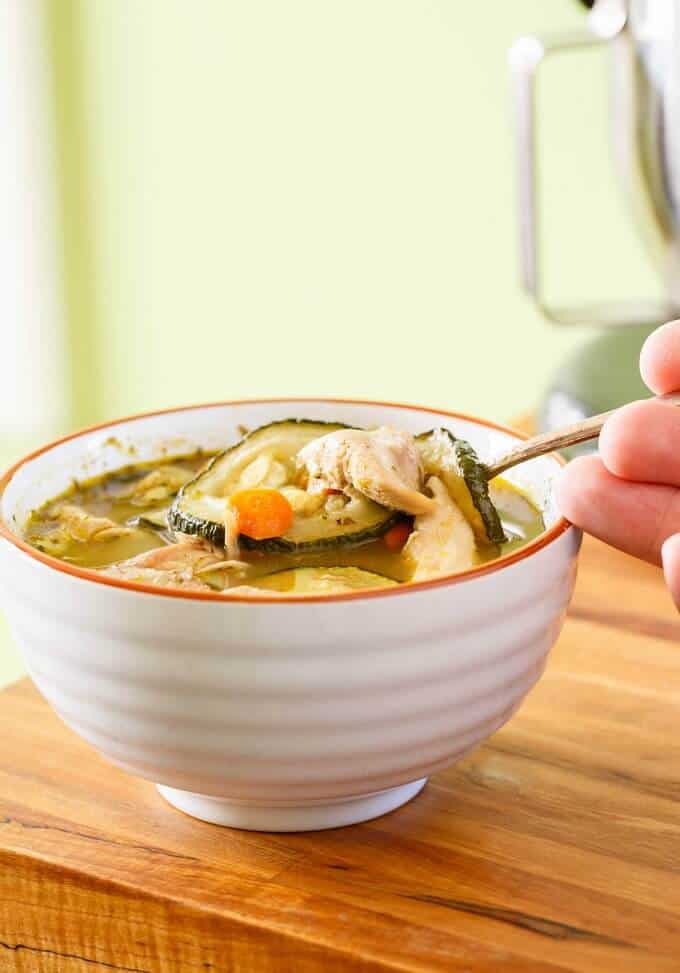 Roasted Zucchini-Carrot Soup in white bowl with spoon held by hand