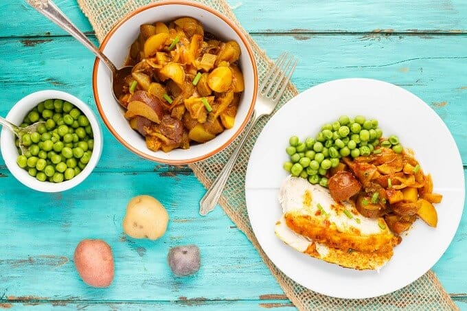 Slow Cooker Curry Chicken on white plate on blue table with bowls of sidedish and vegetables, fork and potatoes