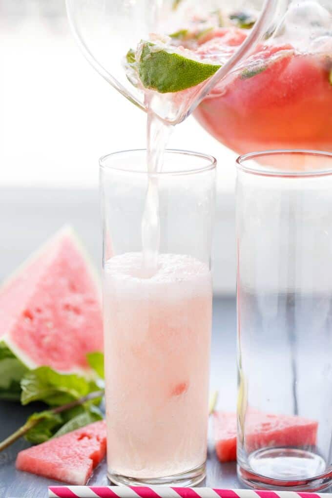 Watermelon Mojitos in glass pitcher poured in glass cups with slices of waterlemon and limes