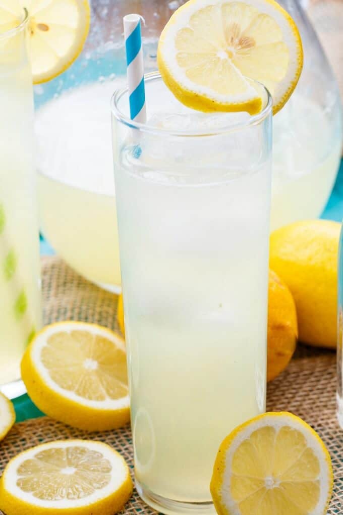 Homemade Roasted Lemonade in glass cup with straw and glass pitcher. Whole  and slices of lemon on the table