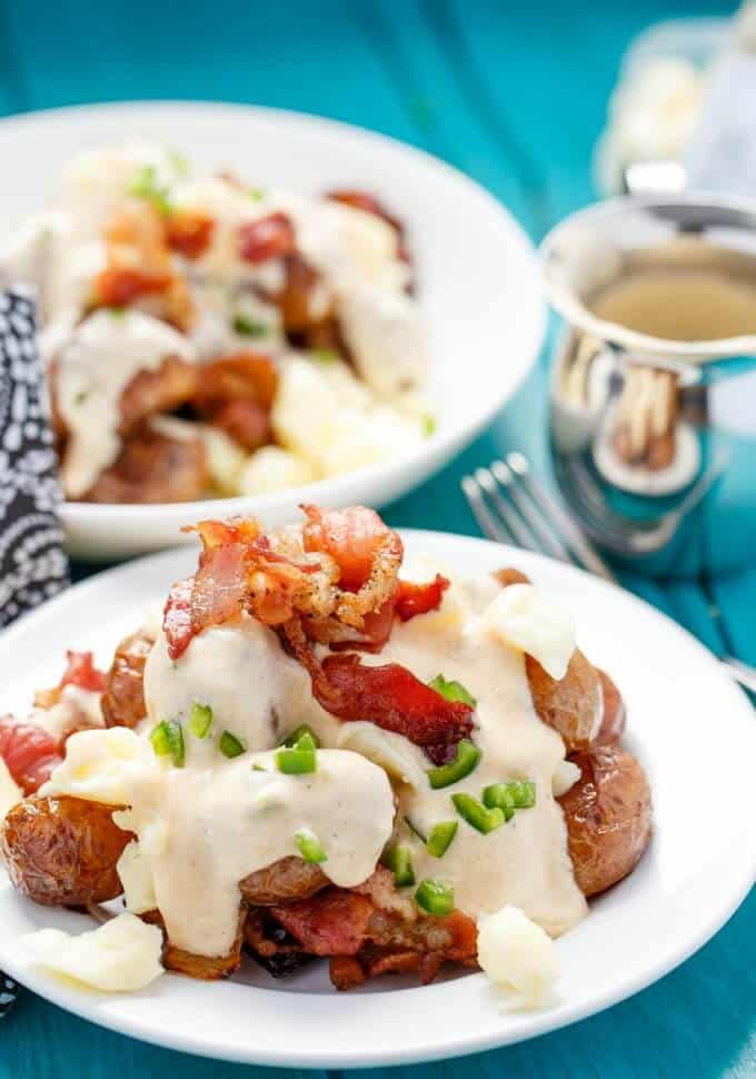 Jalapeno Popper Potato Poutine on white plate and in white bowl on blue table with fork, jar 