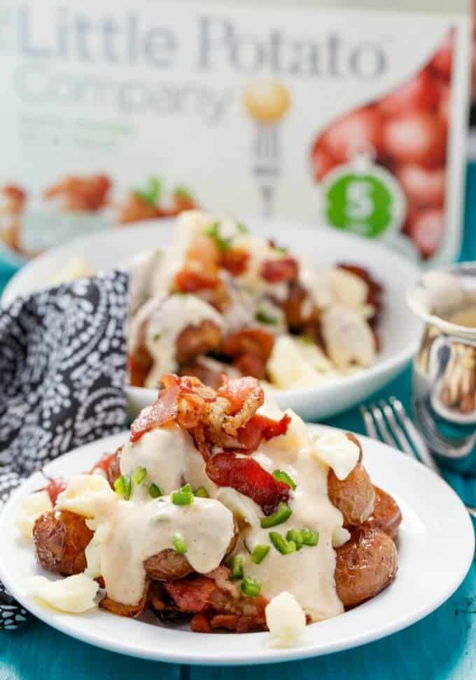 Jalapeno Popper Potato Poutine on white plates on blue table with fork, cloth wipe, jar, little potato company product in the background