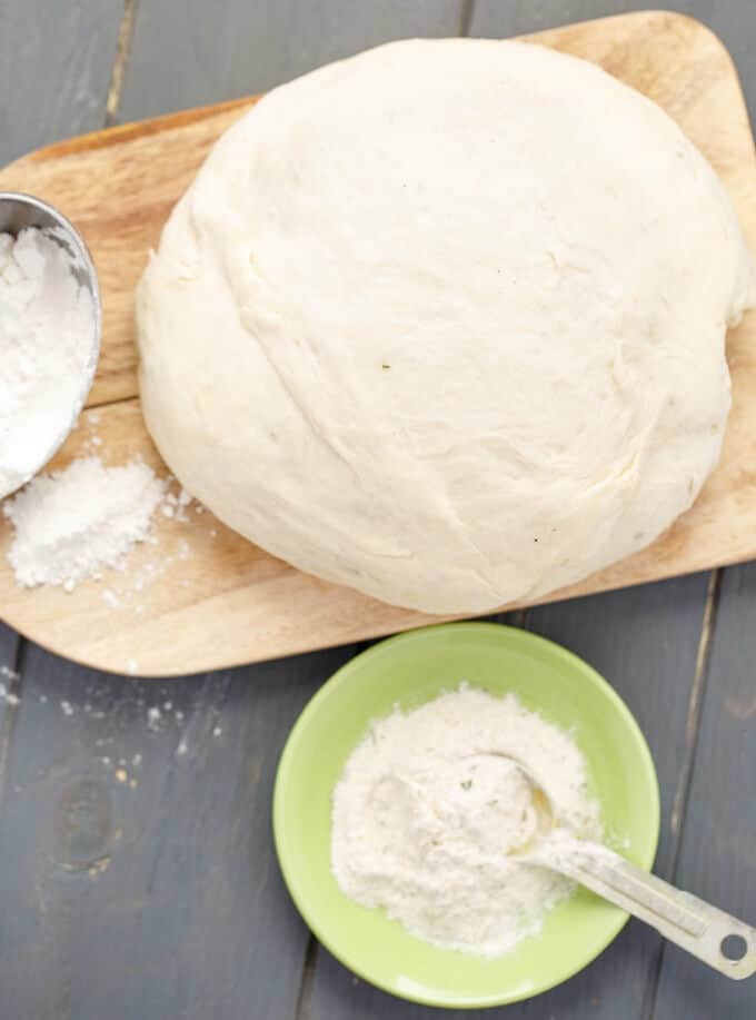 Ranch Pizza Dough on wooden pad nexto to green bowl with flour on gray table