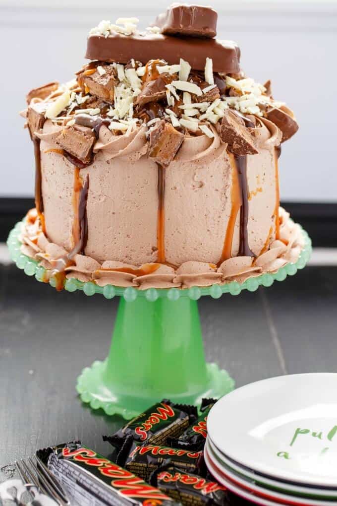 Overloaded Mars Bar Cake (Halloween Leftovers) on green tray on black table with plates, mars bars, fork and spoon