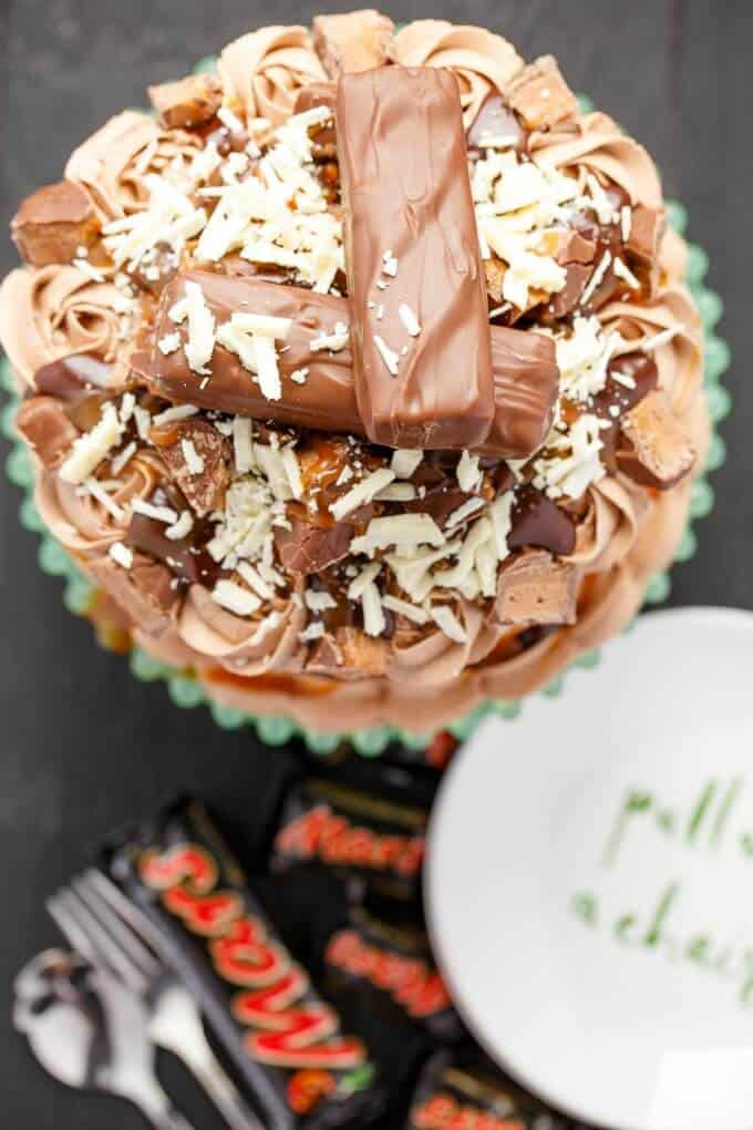 Overloaded Mars Bar Cake (Halloween Leftovers) on black table with fork,spoon, plate and mars bars, top view