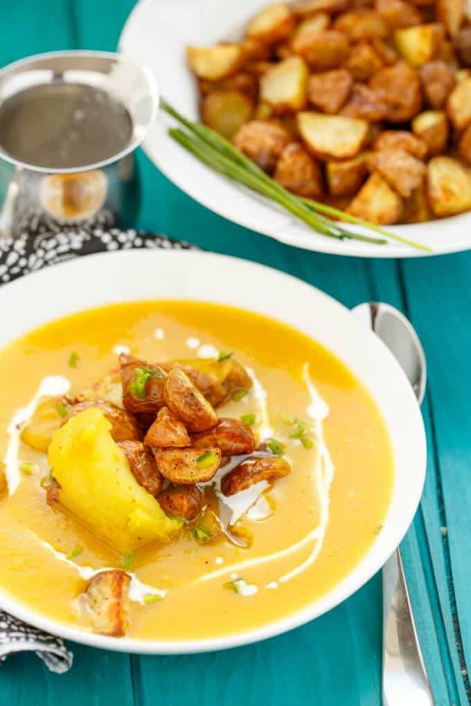 Roasted Apple Pumpkin Soup with Potatoes on white plates on blue table with spoon, jar and plate with potatoes