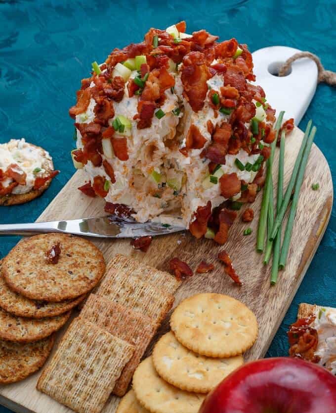 Bacon Apple Cheese Ball on wooden pad with knife, crackers, herbs, red apple