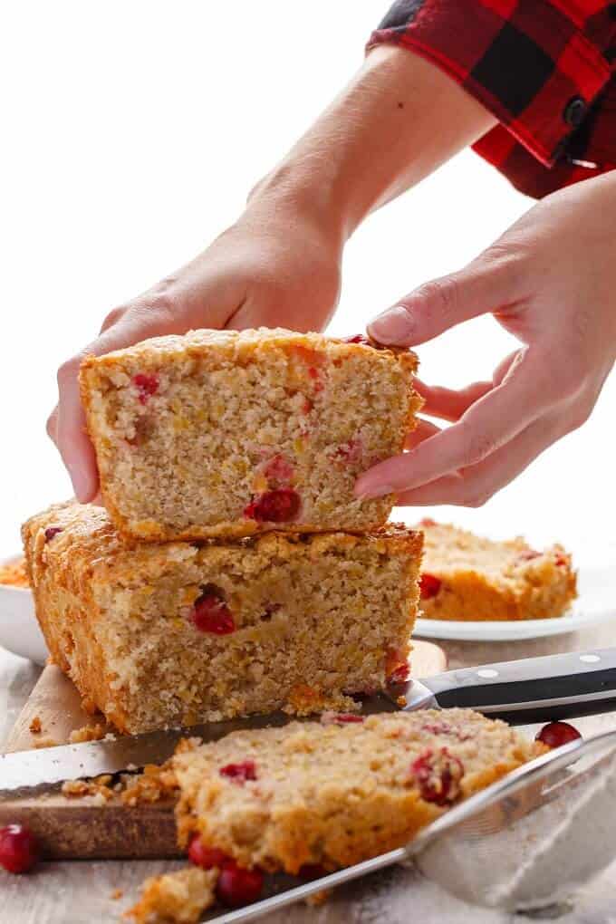 Cranberry Lentil loaf of bread cutted in half on wooden pad held by hand, slices of bread, spilled cranberries,  strainer with flour on the table