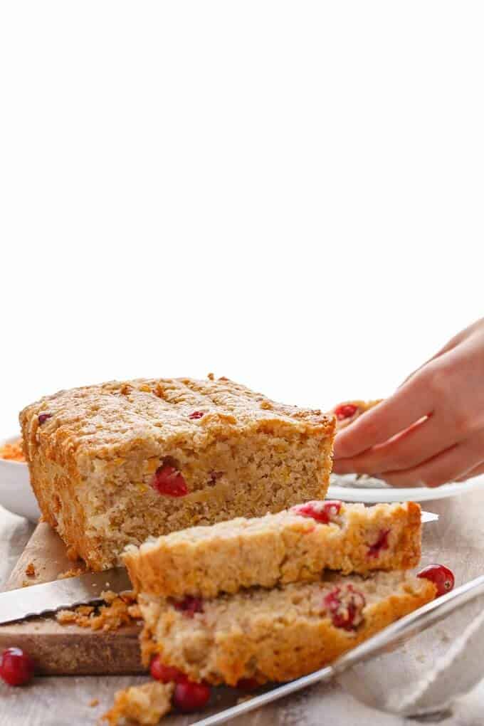 Cranberry Lentil Bread sliced on wooden pad with knife, hand holding slice of bread