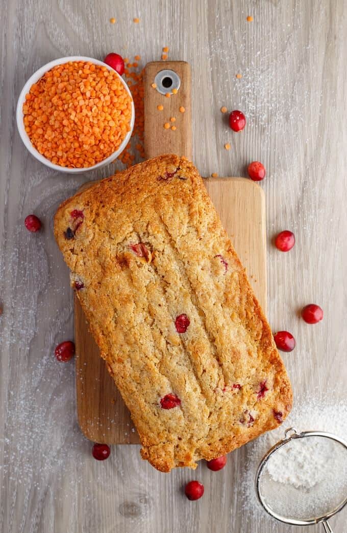 Cranberry Lentil loaf of Bread on wooden pad, spilled cranberries, bowl of lentils and strainer with flour on the table